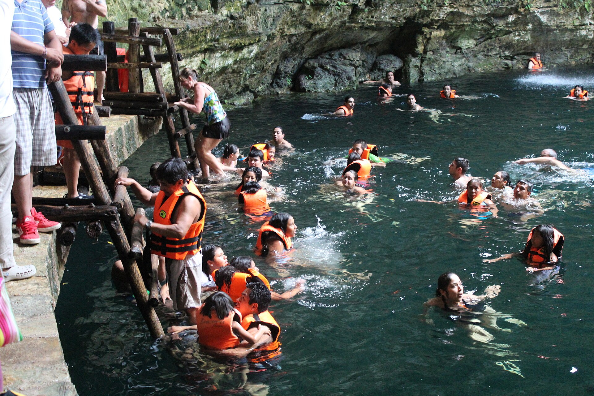 Swimmers in the turquoise water of Cenote Ik Kil surrounded by jungle walls